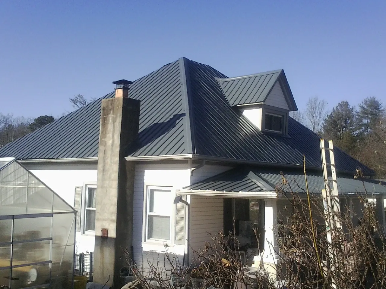Dark blue standing seam metal roof on a white farmhouse with dormer — Slate & Tile Roof Repair by Roofing Brothers in South Seaville