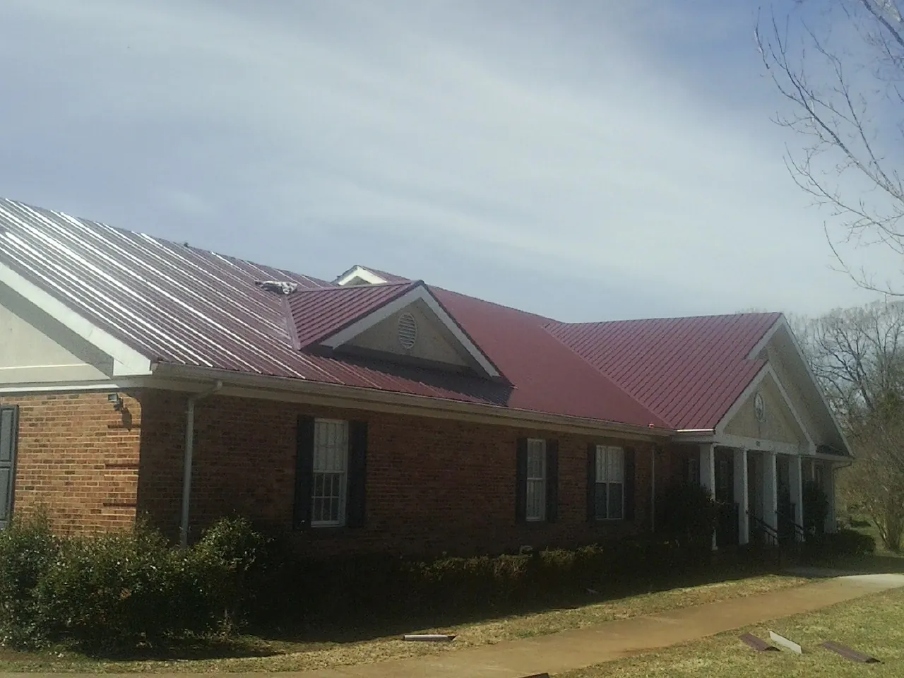 Red metal roof with gabled entries on a long brick building, from a Hail Damage Roof Repair job in South Seaville