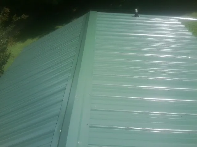 New green metal panels meeting at the ridge of a roof — Flat Roof Repair work by our crew in South Seaville