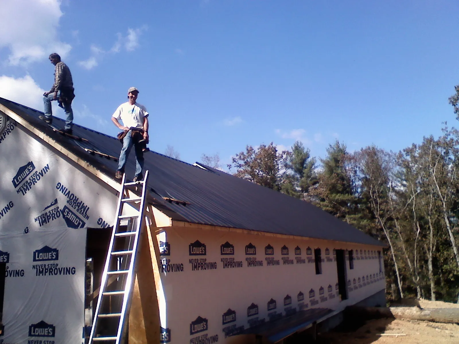 Two roofers standing on a long dark metal roof over a wrapped building in South Seaville