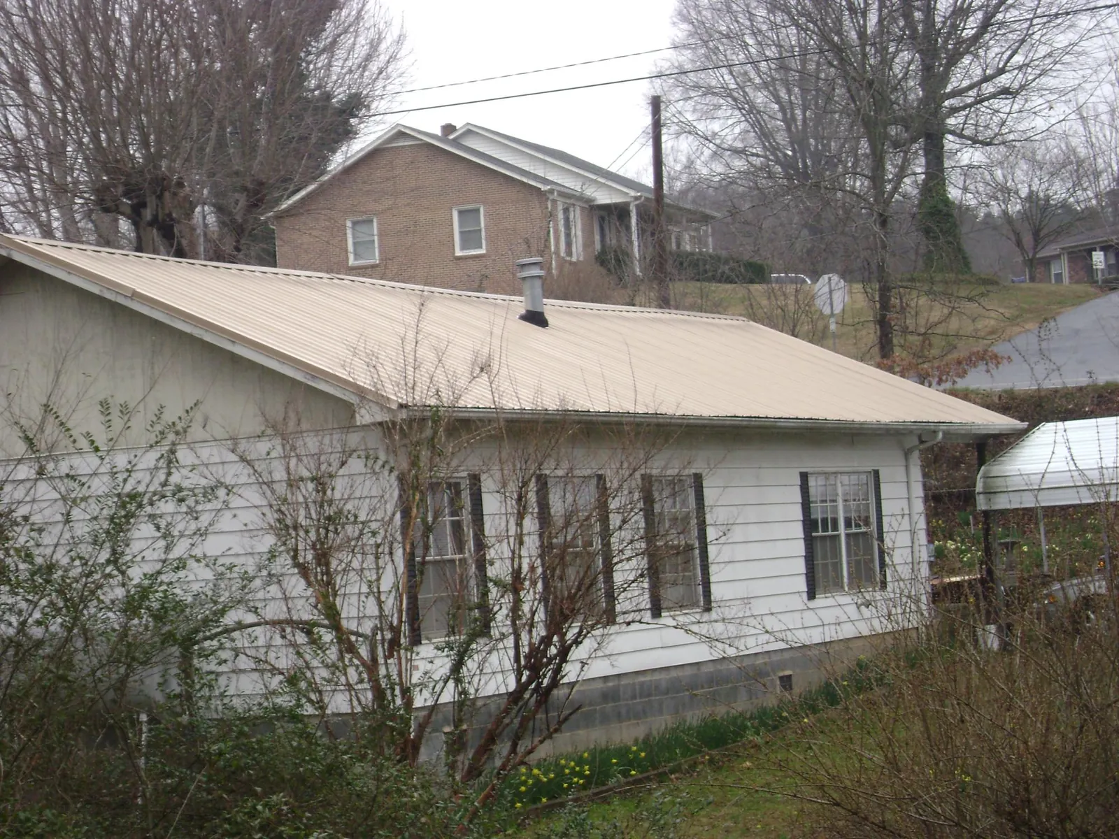 Tan metal roof on a white sided house set into a hillside — Commercial Roofing by Roofing Brothers in South Seaville
